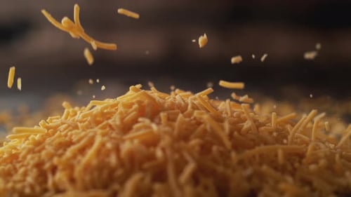 Die Kamera folgt zerkleinertem Cheddar-Käse. Zeitlupe.