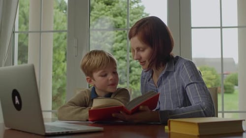 Mother reading book with her child indoors during day