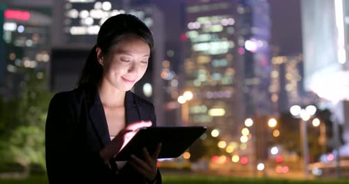 Woman Works on Tablet in City at Night