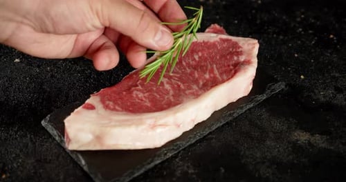A Man's Hand Puts Rosemary on a Steak Striploin Raw.