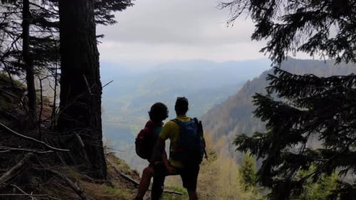 Aerial Flight Over Couple Sitting on Cliff Edge. Young couple hiking on top of the mountai.