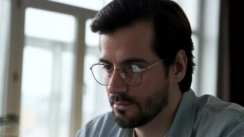 Close Up of a Young man's Face with Glasses Working at a Computer Online Using a Laptop