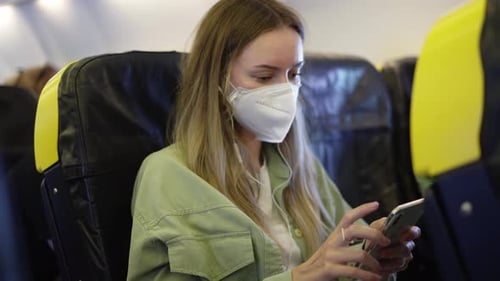 Blonde Woman in the Airplane Listen Music on Earphones Using Mobile Phone During Pandemia