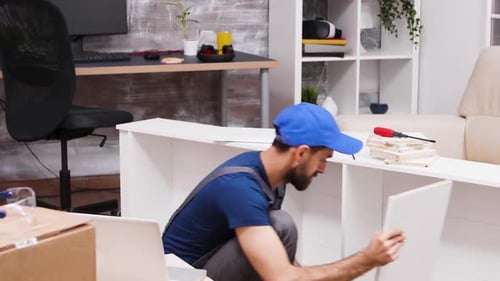 Young Adult Assembles White Shelf Using Laptop Guide