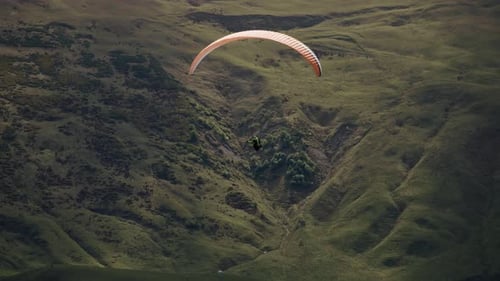 Gleitschirmfliegen neben grünen Berghügeln