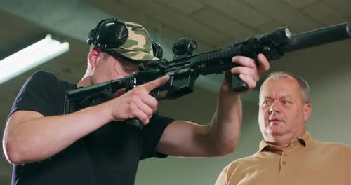 Man Instructing Young Adult with Rifle Indoors