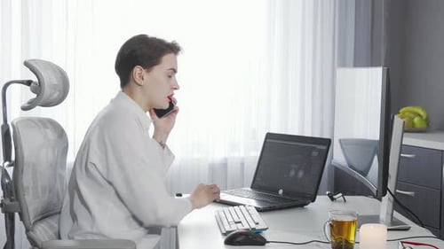 Woman Typing and Talking on Mobile Phone at Desk