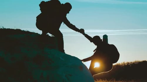 Hikers Helping Each Other Climb Rock At Sunrise