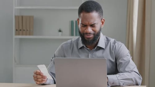 Seriöser schwarzer männlicher Buchhalter, der im Home Office sitzt, arbeitet entfernt und verwaltet die Anzahl der Unternehmensbudgets