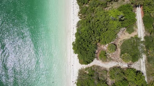 A bird's eye view flying down a secluded beach lined by trees on one side and beach boats on the oth