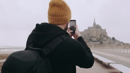 Rear View Happy Excited Tourist Man Taking Smartphone Video of Epic Mont Saint Michel Castle in