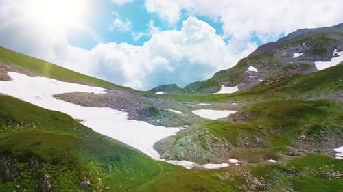 Aerial Flight Over Beauty Caucasian Mountain with Snow Covered By Green Grass Under Cumulus Clouds