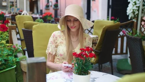 Woman Browsing Smartphone in Outside Cafe. Cheerful Young Lady Sitting at Table in Outside