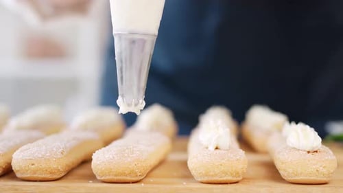 Frauenarme in Uniform, die frische Kekskuchen mit Shake-Up-Zuckerguss versehen, Nahaufnahme