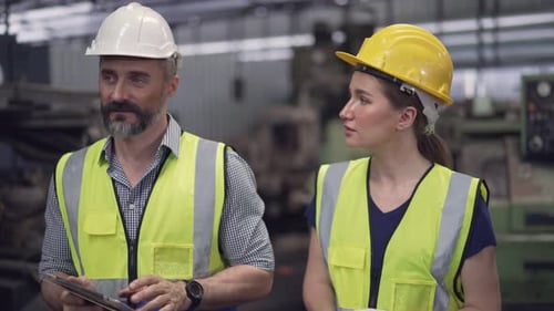 Male engineer foreman with digital tablet walking and talking to female trainee