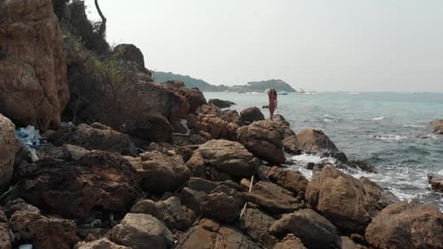 Girl in Bright Red Swimsuit Poses Waving Hands on Rock