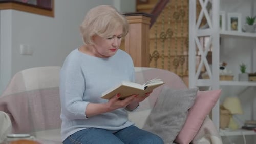 Senior Woman Reading Book on Couch at Home