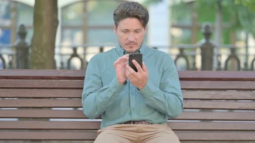 Man Using Phone While Sitting on Park Bench