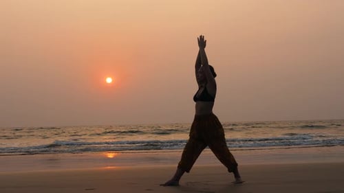 Young Healthy Woman Practicing Yoga on the Beach at Sunset