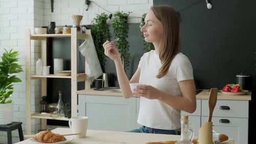 Woman Eating Yogurt for Breakfast in Kitchen
