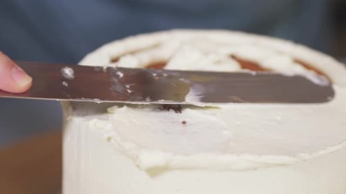 Woman Leveling a Light Cream on a Cake on a Rotating Stand in a Home Kitchen