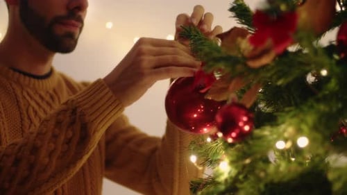 Man Decorating Christmas Tree with Red Ornaments