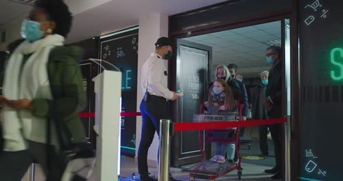 Diverse Crowd Walking Past Guard with Thermometer and Disinfecting Hands in Mall