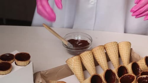 Eine Frau schmiert Waffelkegel mit flüssiger Schokolade. Bringt sie ins Rack.