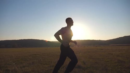 Young Muscular Man Running Through Field with Beautiful Landscape at Background