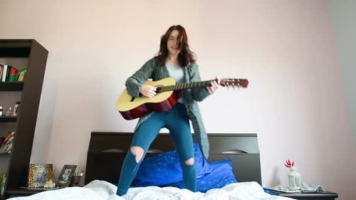 Joven hermosa mujer tocando la guitarra saltando sobre su cama