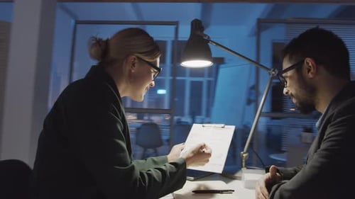 Businesswoman Explaining Project to Male Colleague in Office at Night
