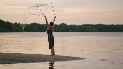 Woman Creates Giant Bubbles on Lake Beach at Sunset