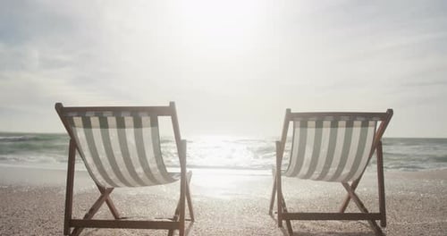 Zwei leere Liegestühle stehen bei Sonnenuntergang am Strand