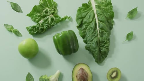 Video of fresh avocado, broccoli, green pepper, apple and green leaves on green background