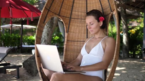 Freelancerin arbeitet remote in einem Cocoon Chair am Strand
