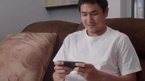 Man Playing Mobile Game on Sofa