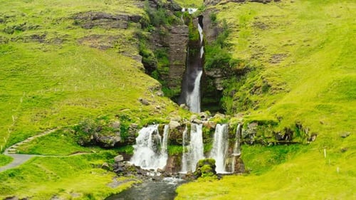 Large Cascade Waterfall Surrounded by Vibrant Green Iceland Backcountry Landscape. HD Aerial Drone.