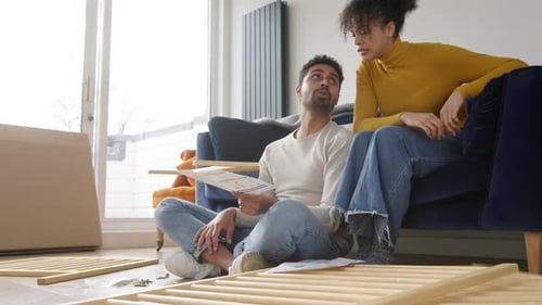 Young Couple In Lounge At Home Reading Instructions For Flat Pack Furniture Assembly