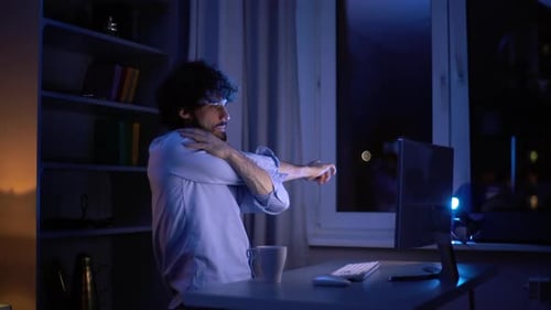 Seitenansicht eines müden Mannes, der sich die Hände vor dem Computer streckt und während der Arbeit in der späten Nacht