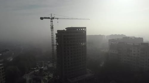 Birds eye view on tower crane in fog standing next to residential building.