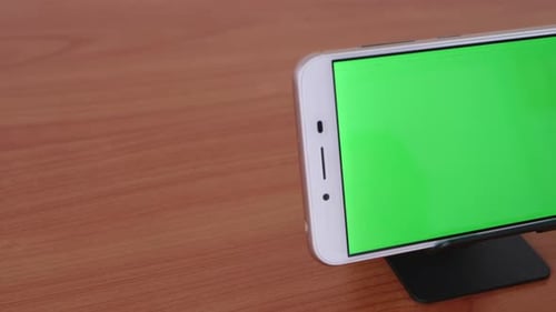 Slide motion of The green screen phone is placed on a pedestal on a wooden table.