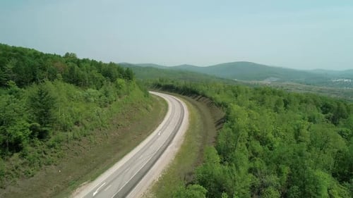 Aerial View of an Asphalt Intercity Country Road Between Green Forest with Vehicles Driving on It