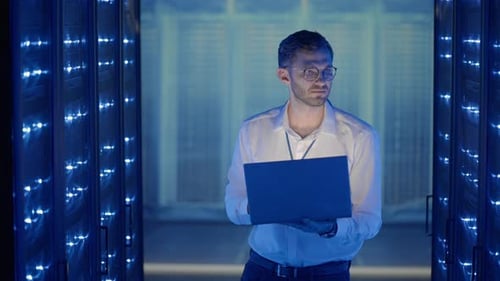 Young Man Works on Laptop in Server Room