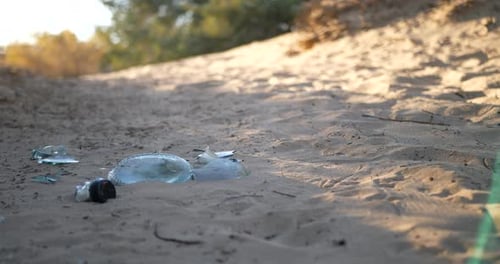 Niedrige Rutschaufnahme einer zerbrochenen Flasche, Müll und Müll auf einem natürlichen Feldwanderweg bei Sonnenaufgang.