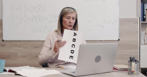 Crop View of Female Teacher Talking and Showing Letters with Pen on Paper Sheet While Looking To