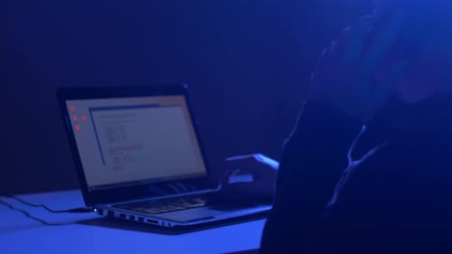 Hacker Typing on Laptop in Blue Lit Room