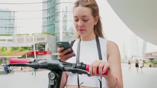 Young Woman Using Phone with Electric Scooter in City
