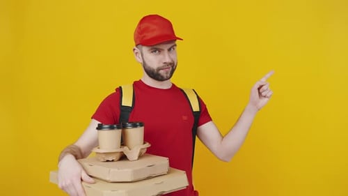 Studio Portrait of Courier in Uniform Holding Food Order and Pointing Aside at Free Space Orange