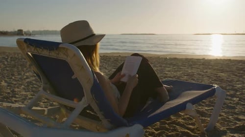 young attractive woman sitting on a beautiful beach reading a book