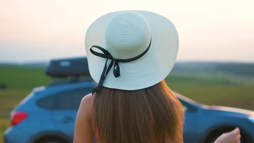 Young Woman Traveler Standing Alone Near Her Car on Green Meadow During Road Trip in Summer